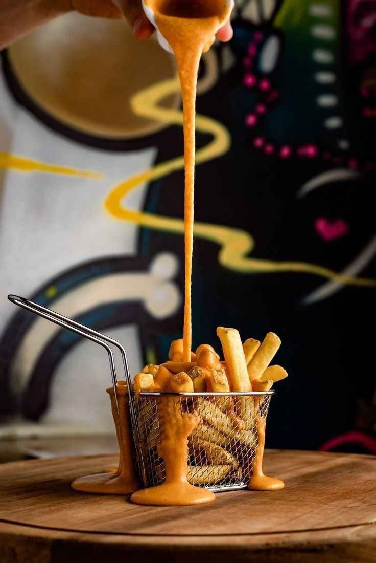 Batata frita em cestinha de metal recebendo uma cascata de cheddar cremoso